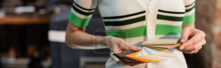 Photo for Cropped view of woman choosing color while holding samples in modern print center, banner - Royalty Free Image