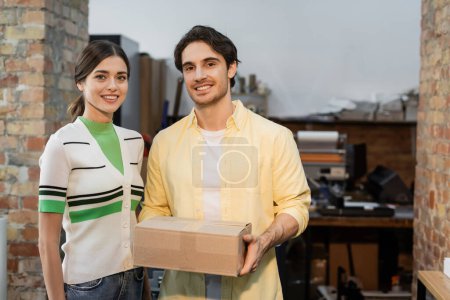 hombre feliz sosteniendo caja de cartón cerca de mujer alegre en el centro de impresión 