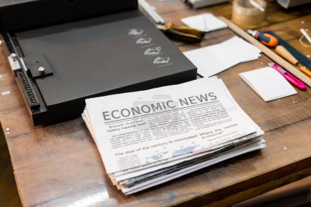 vista de ángulo alto de los periódicos con noticias económicas cerca de la máquina recortadora de papel profesional 