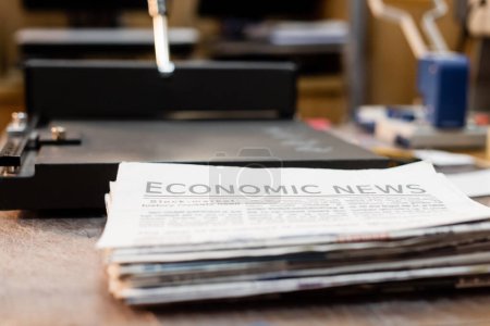 close up view of newspapers with economic news next to professional paper trimmer machine 