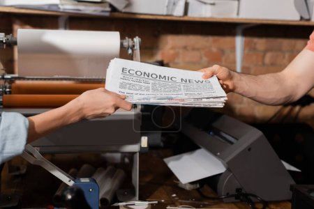 Foto de Vista recortada de tipógrafo dando periódico con letras de noticias económicas a colega en el centro de impresión - Imagen libre de derechos