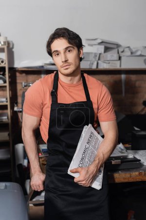 young typographer in apron holding newspapers with economic news  