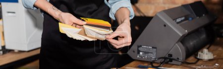 Photo for Cropped view of tattooed typographer in apron choosing color samples in print center, banner - Royalty Free Image