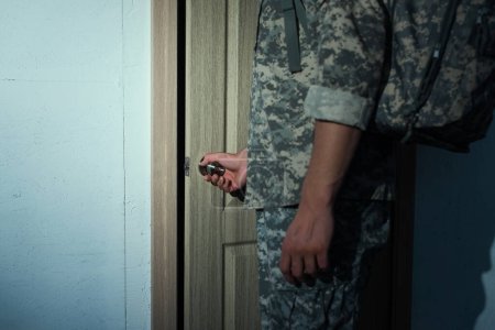 vista recortada del militar en camuflaje apertura de la puerta de casa