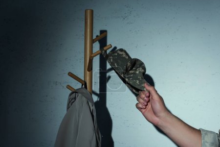 Cropped view of soldier putting cap on floor hanger at home at night 