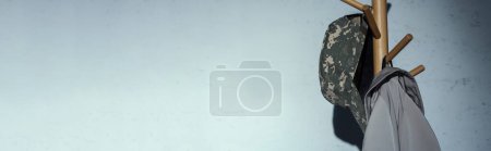 Téléchargez les photos : Casquette militaire avec motif de camouflage suspendue sur le cintre au sol à la maison, bannière - en image libre de droit