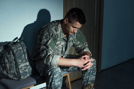 Militärangehöriger in Uniform leidet an posttraumatischer Belastungsstörung, während er zu Hause auf dem Flur sitzt 