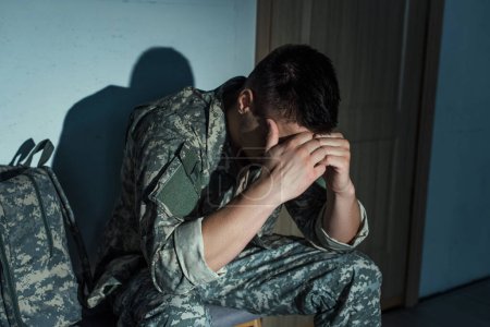 Foto de Veterano militar solitario con trastorno de estrés postraumático sentado en el pasillo en casa por la noche - Imagen libre de derechos