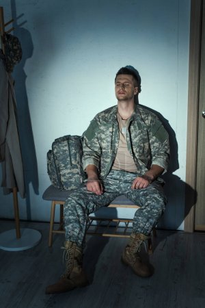 Foto de Veterano militar solitario con trastorno de estrés postraumático sentado en el pasillo en casa por la noche - Imagen libre de derechos