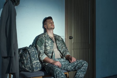 Military soldier with anxiety sitting in hallway on bench at night 