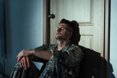 Téléchargez les photos : Vétéran militaire souffrant de troubles mentaux assis près de la porte à la maison la nuit - en image libre de droit