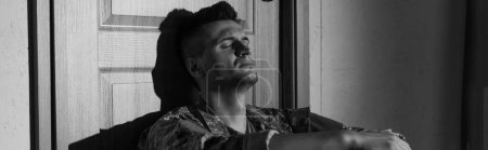 Black and white photo of military veteran with psychological trauma sitting near door at home, banner 
