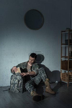 Soldado con el destress mental que toma el marco fotográfico de la mochila en el país en la noche 