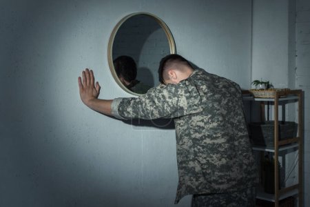 Military veteran with mental illness standing near mirror at home at night 