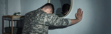 Soldier in uniform with mental problem standing near mirror at home at night, banner 