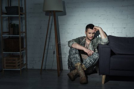 Foto de Deprimido militar veterano en uniforme sentado en el suelo en casa - Imagen libre de derechos