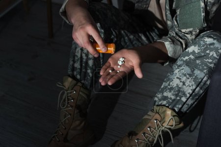 Vue recadrée d'un vétéran militaire versant des pilules sous la main alors qu'il souffrait de détresse émotionnelle à la maison la nuit