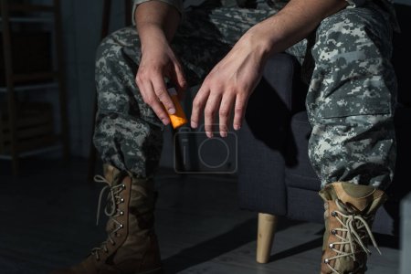 Cropped view of soldier in uniform with ptsd holding antidepressants at home 