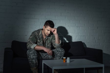 Foto de Veterano militar frustrado con ptsd mirando píldoras en la mesa por la noche - Imagen libre de derechos