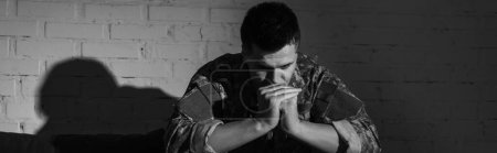 Black and white photo of frustrated military veteran with ptsd problem sitting at home, banner 