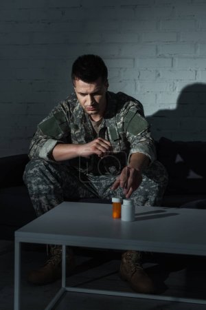 Depressiver Soldat in Uniform nimmt Tabletten von ptsd, während er nachts zu Hause sitzt 