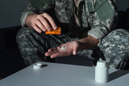 Vista recortada de soldado con trastorno de estrés postraumático sosteniendo pastillas en casa 
