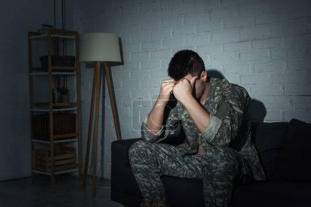 Military veteran in uniform suffering from emotional distress at home at night 