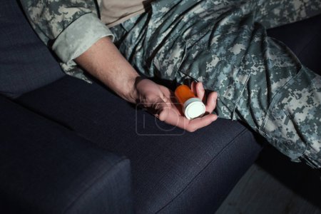 Foto de Vista recortada del soldado con ptsd sosteniendo pastillas en el sofá en casa - Imagen libre de derechos