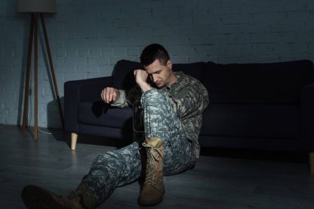 depressed serviceman in military uniform sitting on floor while suffering from post traumatic stress disorder