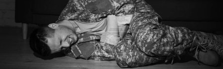 black and while photo of anxious serviceman suffering from post traumatic stress disorder while lying on floor, banner 