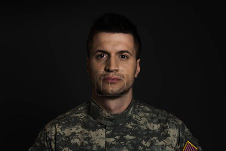 junger Soldat in Uniform, der unter ptsd leidet und isoliert auf schwarz in die Kamera schaut 
