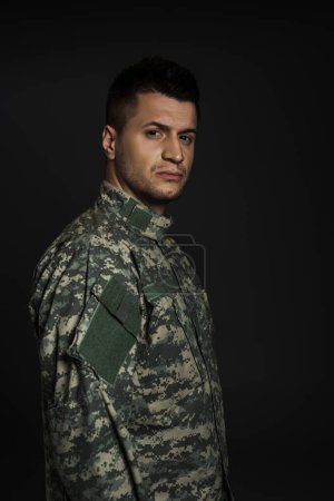 Photo for Depressed soldier in uniform suffering from ptsd isolated on black - Royalty Free Image