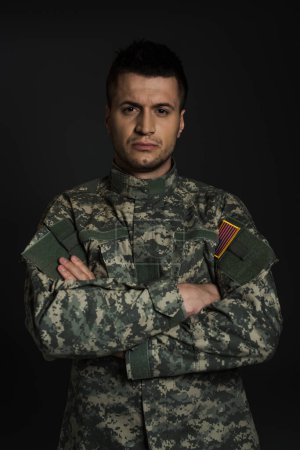 soldat américain déprimé en uniforme debout avec les bras croisés isolés sur noir 