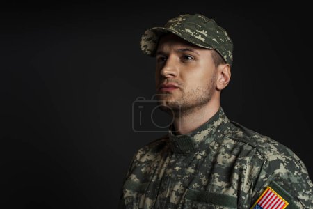 patriotic soldier in uniform with American flag looking away isolated on black 