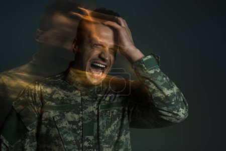 flou de mouvement du soldat en uniforme de camouflage criant tout en souffrant de ptsd isolé sur gris foncé 