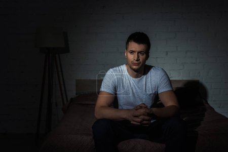 Photo for Depressed man in white t-shirt sitting on bed while suffering from ptsd - Royalty Free Image