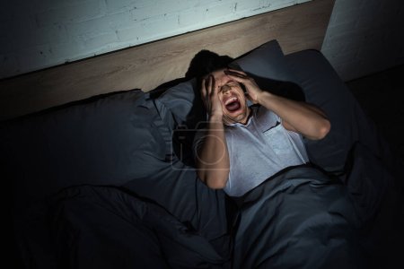 top view of young man screaming while having nightmares and panic attacks at night 