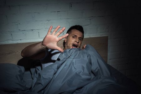 Téléchargez les photos : Homme effrayé avec des attaques de panique hurlant tout couché sous la couverture - en image libre de droit
