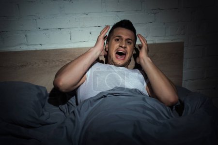 Foto de Estresado hombre con ataques de pánico gritando mientras tiene pesadilla en la noche - Imagen libre de derechos