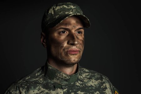 Foto de Soldado con suciedad en la cara de pie en uniforme y gorra que sufre de ptsd aislado en gris - Imagen libre de derechos