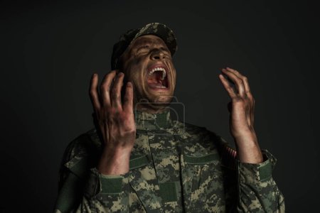 Photo for Military man with dirt on face screaming while suffering from ptsd isolated on grey - Royalty Free Image