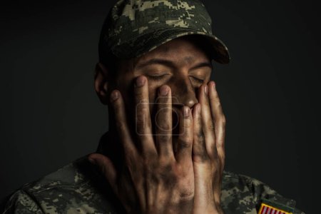 Militärangehöriger mit geschlossenen Augen, der das Gesicht mit schmutzigen Händen bedeckt und unter ptsd isoliert auf grau leidet 