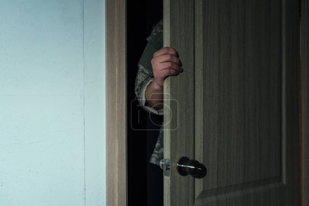 Foto de Vista recortada del militar en uniforme militar abriendo la puerta mientras entra en la habitación - Imagen libre de derechos