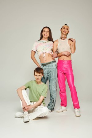 Diverse group of happy young lgbt community friends in colorful clothes smiling while celebrating pride month together and looking at camera on grey background in studio 