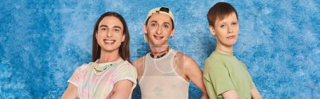 Overjoyed young homosexual community looking at camera together while celebrating lgbt pride month and standing on mottled blue background, banner 