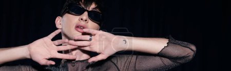 Photo for Portrait of young, tattooed and fashionable gay man in sunglasses and sparking top posing during lgbt pride month party isolated on black, banner - Royalty Free Image