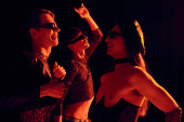 Side view of smiling and trendy homosexual people in sunglasses and party clothes dancing during celebration of lgbt pride month isolated on black with red lighting  magic mug #656051362
