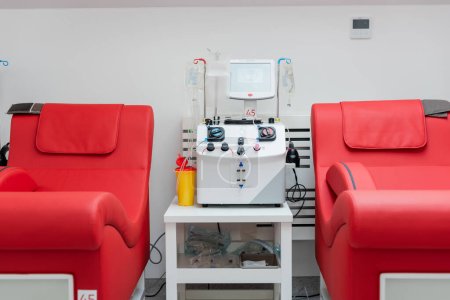 Foto de Sillas médicas con diseño ergonómico cómodo cerca de la máquina de transfusión automatizada, pantalla táctil, taza de plástico y soportes de goteo con bolsas de infusión en el centro de donación de sangre - Imagen libre de derechos