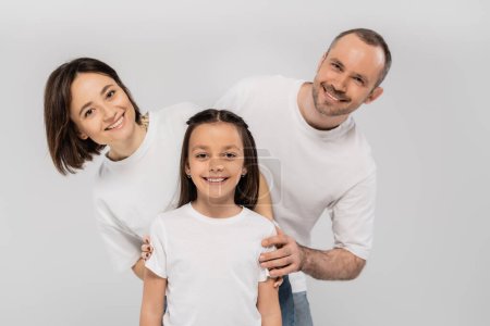 happy family in white t-shirts looking at camera and posing together on grey background, International child protection day, positive father mother and daughter 