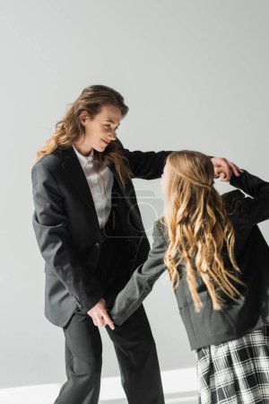 Photo for Fashionable mother and daughter, woman in suit holding hands with schoolgirl in school uniform with plaid skirt, blazers, businesswoman, getting ready for new school year, having fun - Royalty Free Image